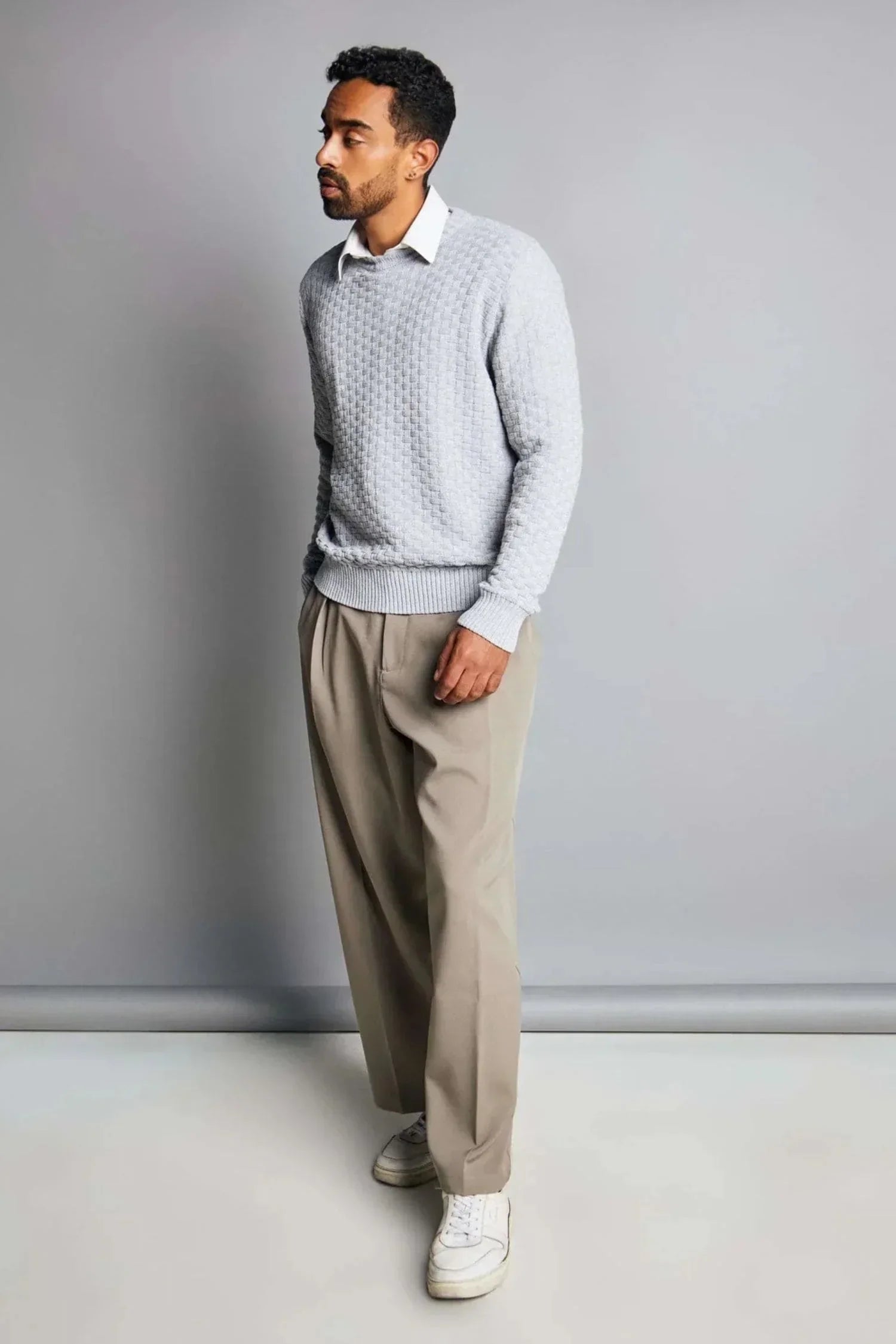 Hombre con suéter gris tejido, pantalón beige y tenis blancos, ropa casual de punto para hombre